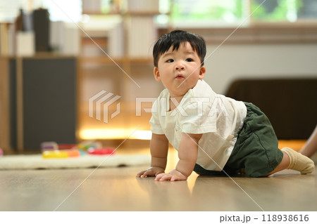 Adorable baby boy crawling on the floor in living room, exploring his surroundings. Child development concept Adorable baby boy crawling on the floor in living room, exploring his surroundings. Child development concept 118938616