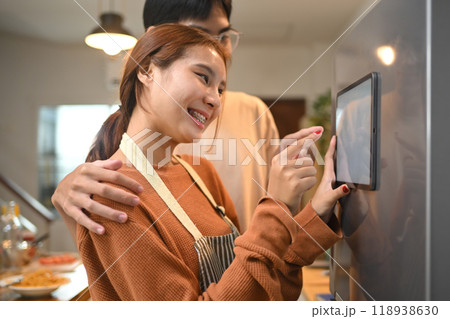 Happy young couple using a touchscreen on smart refrigerator at modern home Happy young couple using a touchscreen on smart refrigerator at modern home 118938630