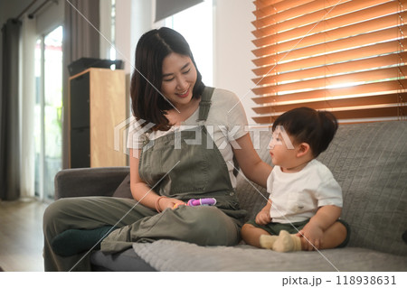 Delightful young mother playing with baby boy on sofa. Family and childcare concept Delightful young mother playing with baby boy on sofa. Family and childcare concept 118938631