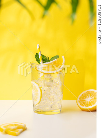 A glass of cold lemonade with lemon, mint and ice on a yellow and white background A glass of cold lemonade with lemon, mint and ice on a yellow and white background 118938711