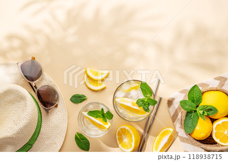 Summer layout with lemonade, citrus fruits, hat and sunglasses on a beige background with shadows. Summer layout with lemonade, citrus fruits, hat and sunglasses on a beige background with shadows. 118938715