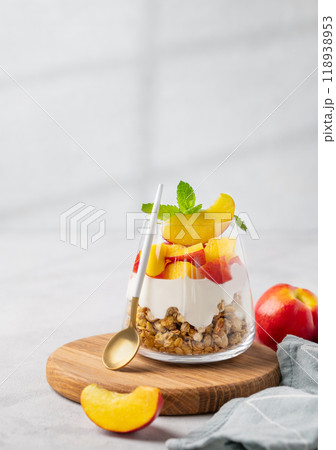 Greek yogurt parfait with peach and muesli in a glass on a wooden board on a light background Greek yogurt parfait with peach and muesli in a glass on a wooden board on a light background 118938953