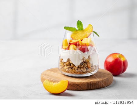 Yogurt parfait with peach and granola in a glass on a wooden board on a light background Yogurt parfait with peach and granola in a glass on a wooden board on a light background 118938954