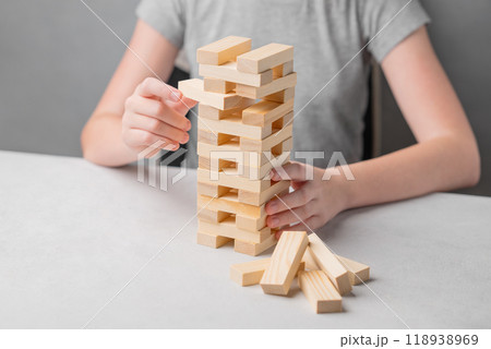 A child sits at a table and with his hand pulls out a piece from a wooden tower game  118938969