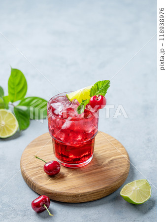 Cherry-lime mojito cocktail with mint, lime and ice on a wooden board on a blue background. Cherry-lime mojito cocktail with mint, lime and ice on a wooden board on a blue background. 118938976