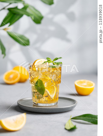 Iced tea with lemon, mint and ice in a glass on a light background with shadow and branch. Iced tea with lemon, mint and ice in a glass on a light background with shadow and branch. 118939018