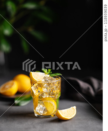 A glass of iced tea with lemon and mint on a dark background with citrus fruits and branch. A glass of iced tea with lemon and mint on a dark background with citrus fruits and branch. 118939039