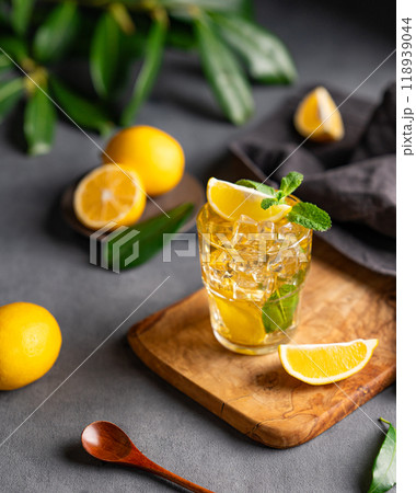 A glass of iced tea with lemon and mint on a wooden board on a dark background with citrus fruits 118939044