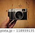 クラシックデザインのデジタルカメラを手に取ったPOV — 新製品と美しいパイン材の背景 クラシックデザインのデジタルカメラを手に取ったPOV — 新製品と美しいパイン材の背景 118939135