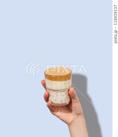 Dalgona coffee. A hand holds a glass of whipped and instant iced coffee and milk in a glass  118939137