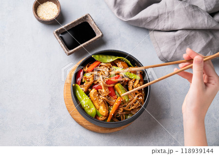 Stir-fry with soba noodles, meat and vegetables in black plate on a light background Stir-fry with soba noodles, meat and vegetables in black plate on a light background 118939144