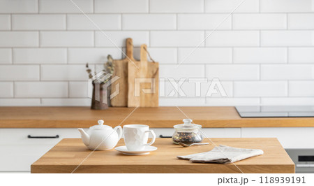Wooden oak table with a cup of tea and a kettle in front of the kitchen with white brick background Wooden oak table with a cup of tea and a kettle in front of the kitchen with white brick background 118939191