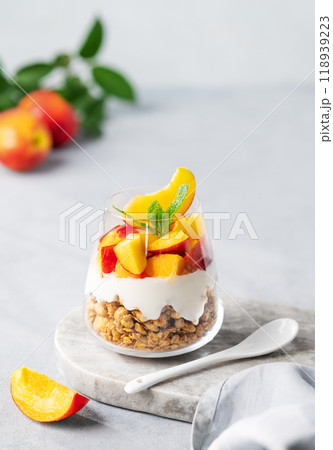 Yogurt parfait with peach and granola in a glass on a marble board on a light background Yogurt parfait with peach and granola in a glass on a marble board on a light background 118939223