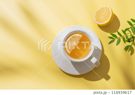 Herbal tea with lemon in a white cup on a yellow background with shadows. 118939617