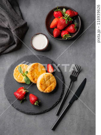 Cottage cheese, cheesecakes or syrniki with sour cream, strawberries and mint leaves on black slate Cottage cheese, cheesecakes or syrniki with sour cream, strawberries and mint leaves on black slate 118939626
