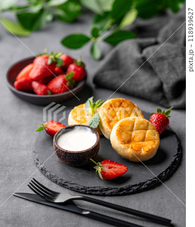 Cottage cheese, cheesecakes or syrniki with sour cream, strawberries and mint leaves on black slate 118939627