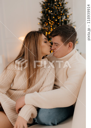 Happy couple celebrating romantic Christmas eve at home. Christmas interior decoration for family party. Copy space, greeting card. Middle-aged man and woman sitting on cozy bed with knitted blanket Happy couple celebrating romantic Christmas eve at home. Christmas interior decoration for family party. Copy space, greeting card. Middle-aged man and woman sitting on cozy bed with knitted blanket 118939914