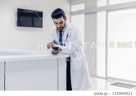 doctor in white coat Standing using cellphone applications in clinic office. Man with healthcare, medical and wellness app on mobile technology or search internet doctor in white coat Standing using cellphone applications in clinic office. Man with healthcare, medical and wellness app on mobile technology or search internet 118940021