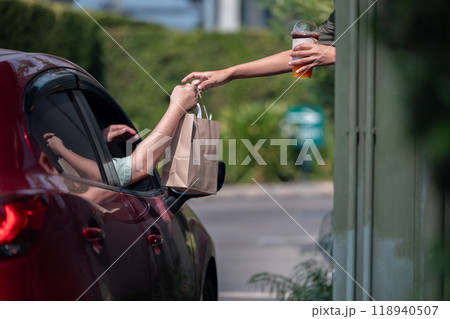 Hand Man in car receiving coffee in drive thru fast food restaurant. Staff serving takeaway order for driver in delivery window. Drive through and takeaway for buy fast food for protect covid19. 118940507
