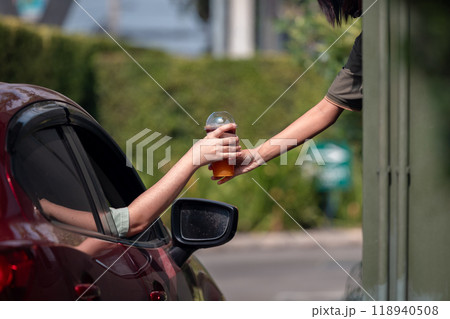 Hand Man in car receiving coffee in drive thru fast food restaurant. Staff serving takeaway order for driver in delivery window. Drive through and takeaway for buy fast food for protect covid19. 118940508