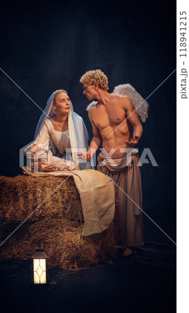 Christmas nativity scene with Mary holding baby Jesus and angel standing near against black background. Holy night. 118941215