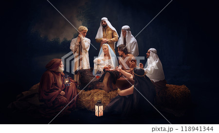 Nativity setup with newborn child, Jesus, cradled by Mary. Shepherd with lantern highlights warmth and wonder of sacred moment. 118941344