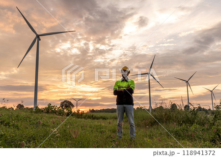 Professional Man Maintenance engineers working in wind turbine farm at sunset.  Engineer Man standing among Wind Energy Turbine. 118941372