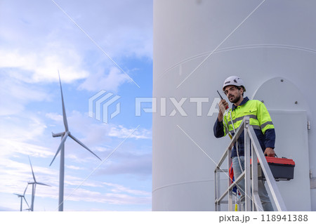 Professional Man Maintenance engineers working in wind turbine farm at sunset.  Engineer Man standing among Wind Energy Turbine. 118941388