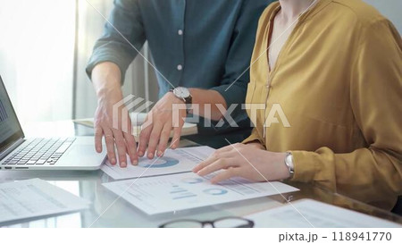 Team collaboration over financial reports. Close-up view of two business people, professionals analyzing financial charts and data on a desk near a laptop computer Team collaboration over financial reports. Close-up view of two business people, professionals analyzing financial charts and data on a desk near a laptop computer 118941770