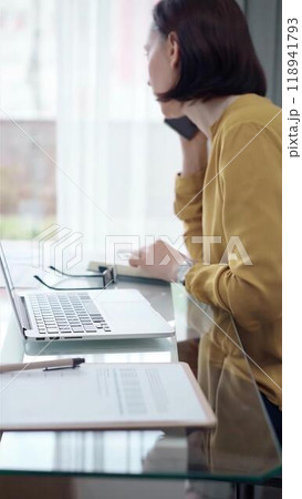 Young professional woman is talking by smartphone in modern office. Yellow blouse is passing to adult businesswoman. Business people concept Young professional woman is talking by smartphone in modern office. Yellow blouse is passing to adult businesswoman. Business people concept 118941793