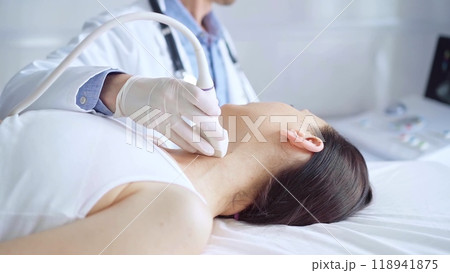 Doctor man is using ultrasound equipment on neck of female patient lying down for a medical examination. Medicine and science Doctor man is using ultrasound equipment on neck of female patient lying down for a medical examination. Medicine and science 118941875