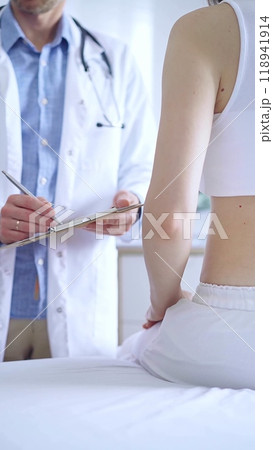 Doctor and patient. Physician is making notes on a clipboard while patient woman is describing something. Pediatrician, medicine concept 118941914