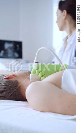 Doctor woman with green medical gloves performing neck ultrasound exam on male patient. Thyroid gland examination. Medicine concept 118941945
