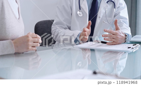 Doctor consulting patient. Male physician is gesturing above a clipboard while talking with a woman in a clinic, close up. Medicine concept 118941968