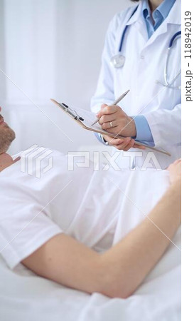 Female doctor writing medical report of patient lying in bed in hospital Female doctor writing medical report of patient lying in bed in hospital 118942019