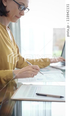 Adult professional woman is working with laptop in flair office. Yellow blouse is passing to adult businesswoman, vertical portrait. Business people concept 118942131