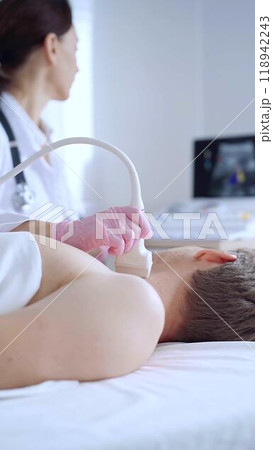 Doctor woman with pink medical gloves performing neck ultrasound exam on male patient. Thyroid gland examination. Medicine concept 118942243