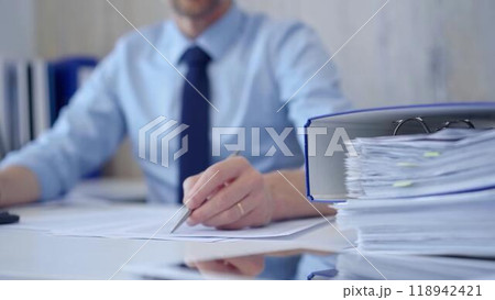 Unknown man accountant with blue t-shirt concentrating while calculating costs and taking notes at his desk. Taxes, audit in business Unknown man accountant with blue t-shirt concentrating while calculating costs and taking notes at his desk. Taxes, audit in business 118942421