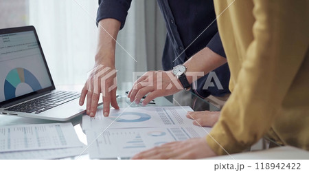 Business people, professionals analyzing financial charts and data on a desk while standing and using laptop computer in office. Dark blue shirt and yellow blouse Business people, professionals analyzing financial charts and data on a desk while standing and using laptop computer in office. Dark blue shirt and yellow blouse 118942422