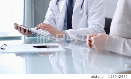 Doctor is consulting patient in modern clinic. Healthcare professional discusses medical information with a woman, using a tablet computer. Medicine concept 118942432