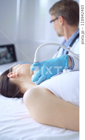 Doctor man wearing blue protective gloves is using ultrasound equipment on the neck of a patient woman, lying for examination. Medicine concept Doctor man wearing blue protective gloves is using ultrasound equipment on the neck of a patient woman, lying for examination. Medicine concept 118942485