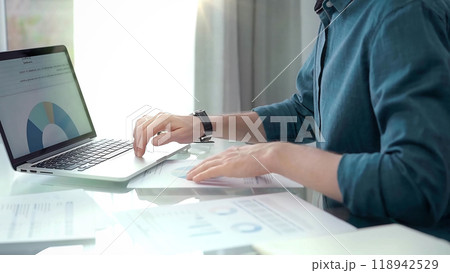 Professional working at laptop with data analysis charts. Businessman analyzing statistical data on a laptop next to business reports. Business concept Professional working at laptop with data analysis charts. Businessman analyzing statistical data on a laptop next to business reports. Business concept 118942529
