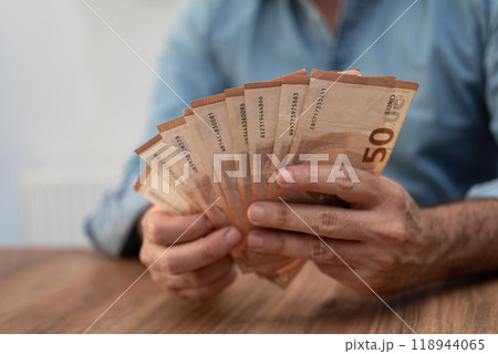 Person fanning out 50 euro banknotes on a wooden table. Depicts financial transactions, currency management, and economic stability  118944065