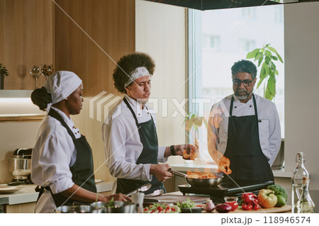 Male cook cooking steak in flambe style while his colleagues looking at flame 118946574