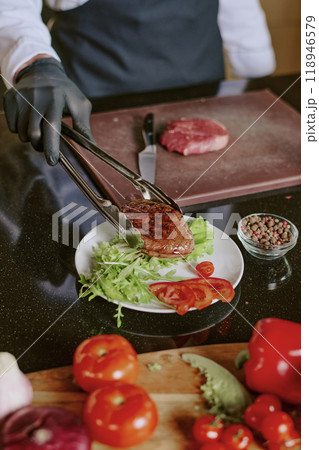 Vertical high angle shot of unrecognizable cooks hands serving dish with grilled beef steak Vertical high angle shot of unrecognizable cooks hands serving dish with grilled beef steak 118946579
