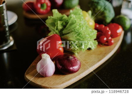 Medium close up of fresh vegetables and green on shaped wooden plate Medium close up of fresh vegetables and green on shaped wooden plate 118946728