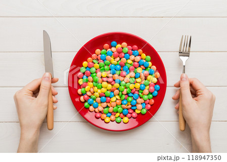 the girl holds cutlery in her hands and eats sweets in a plate. Health and obesity concept, top view on colored background the girl holds cutlery in her hands and eats sweets in a plate. Health and obesity concept, top view on colored background 118947350
