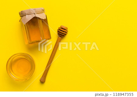 Glass jar of honey with wooden drizzler on colored background. Honey pot and dipper high above. Top view copy space 118947355