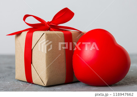 gift box with red bow and red heart on colored background. Perspective view. Flat lay gift box with red bow and red heart on colored background. Perspective view. Flat lay 118947662