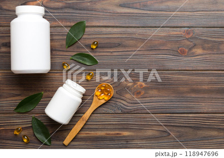 Omega-3 capsules lie in white bottle on a table with green leaves background. Fish oil tablets. Biologically active additives. omega 6, omega 9, vitamin A, E, D, vitamin D3 top view with copy space 118947696